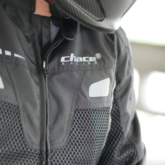 Close-up of the rider's chest area wearing the black Volt jacket, prominently featuring the white "Chace Racing" logo, the front zipper, and the hexagonal breathable mesh fabric panel.