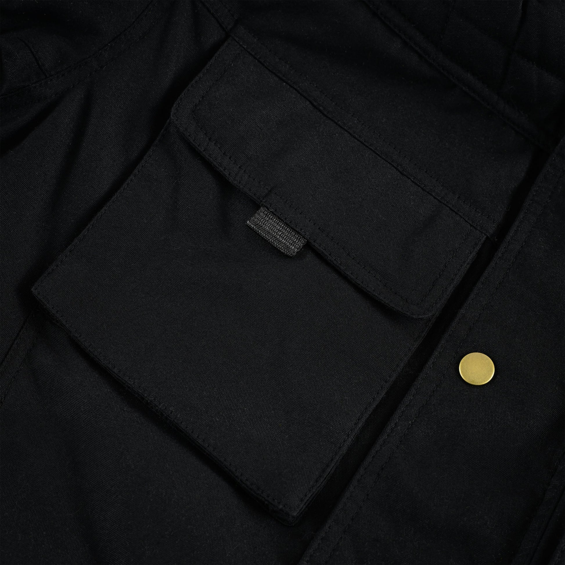 Extreme close-up of the large black flap pocket on the jacket's chest, showing the neat stitching, rectangular flap shape, and the secure, hidden fastening tab.