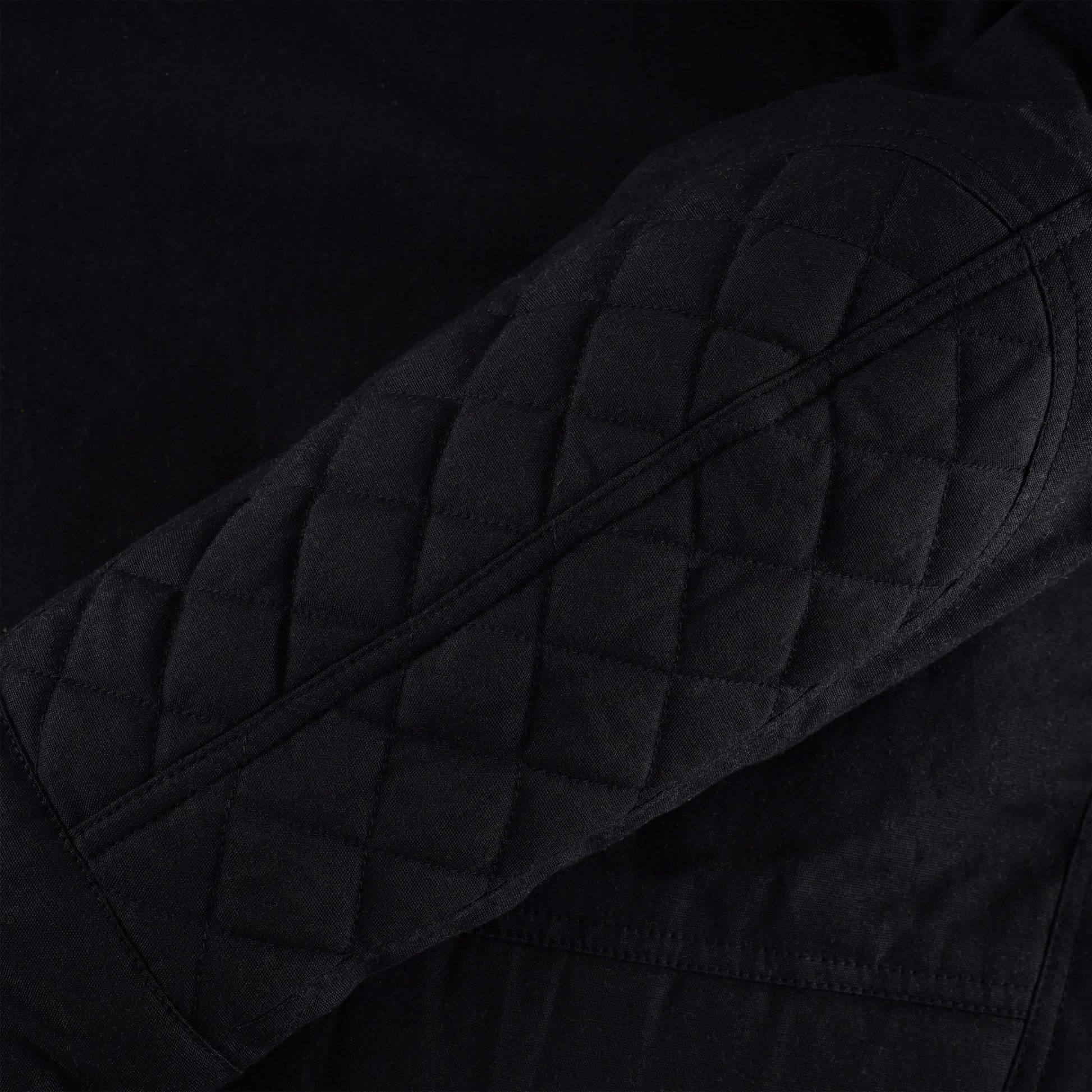 A close-up detail shot focusing on the quilted, diamond-stitched padding on the elbow area of the black motorcycle jacket sleeve.