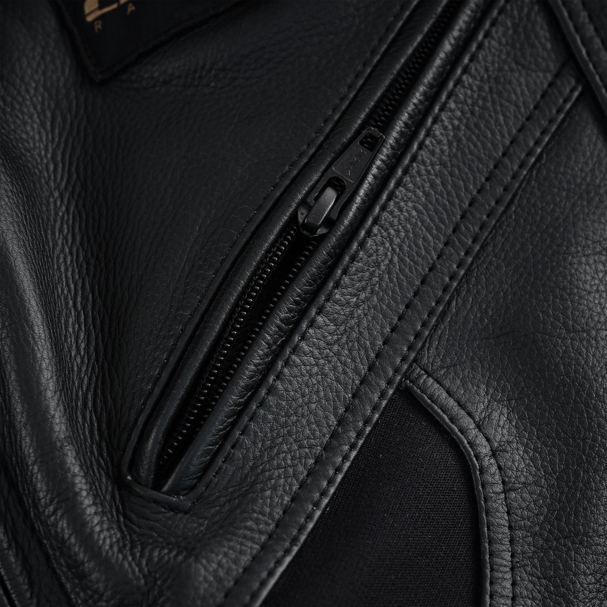 Close-up of a zippered pocket set into the black leather of the motorcycle trousers, highlighting the zipper track and the leather texture.