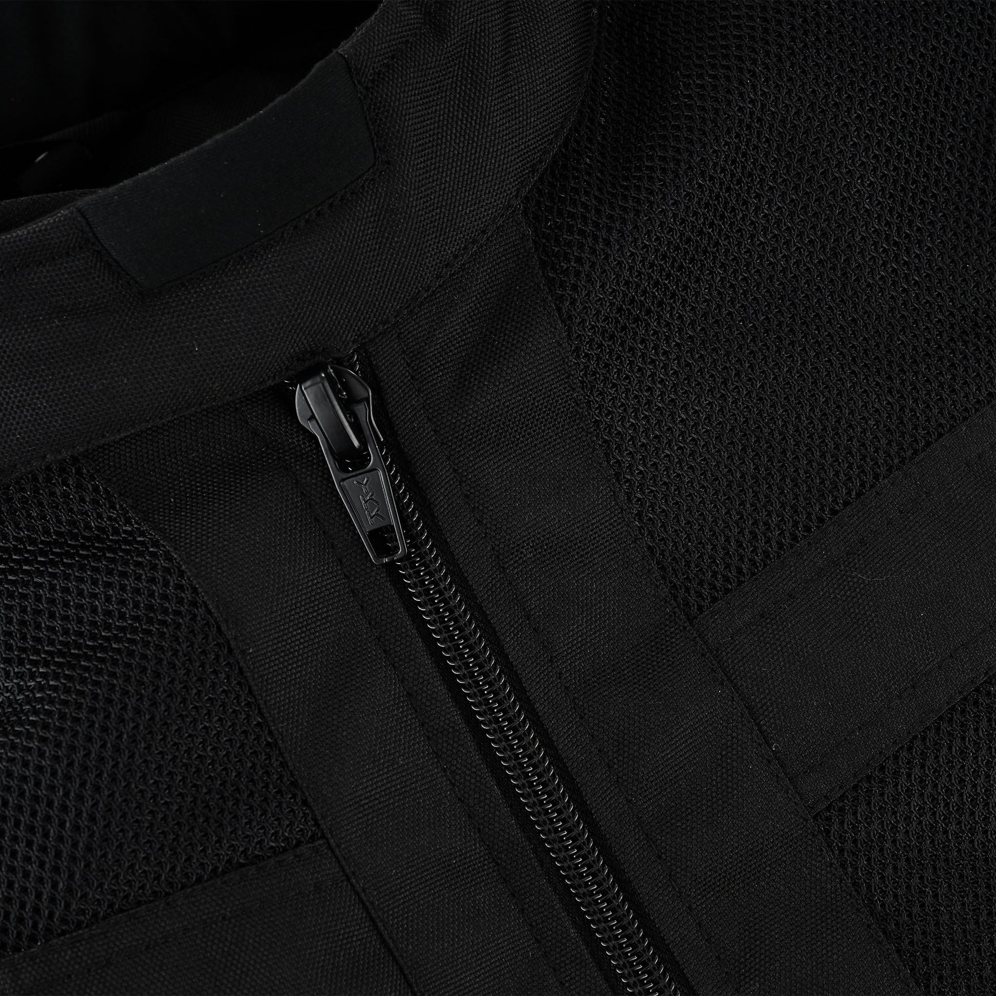 Extreme close-up of a heavy-duty black YKK zipper track and pull tab, set into the textile material adjacent to the black breathable mesh panel.