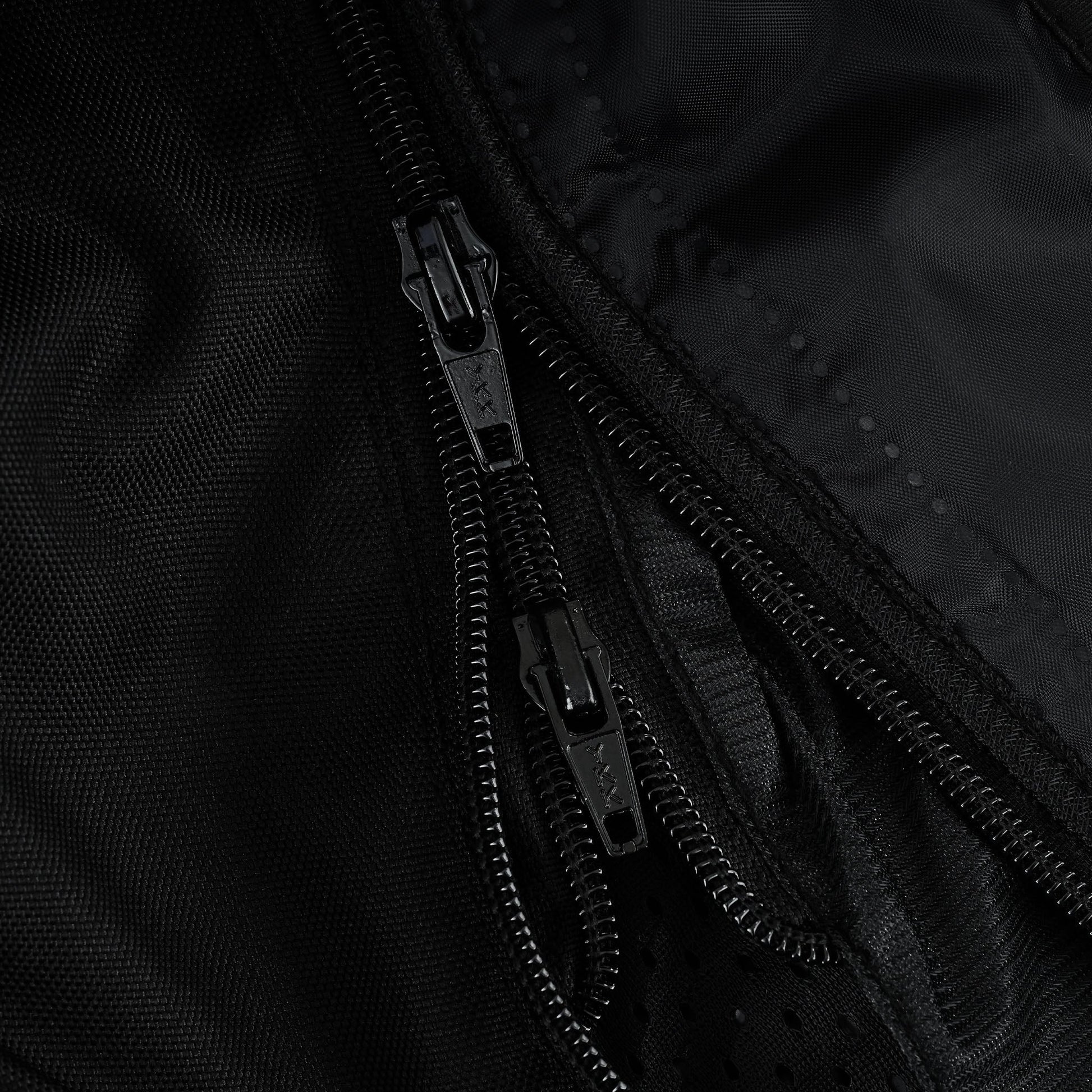 Extreme close-up of two parallel heavy-duty black zippers with marked pull tabs, likely indicating a double closure system for water resistance or the main zipper and liner zipper.
