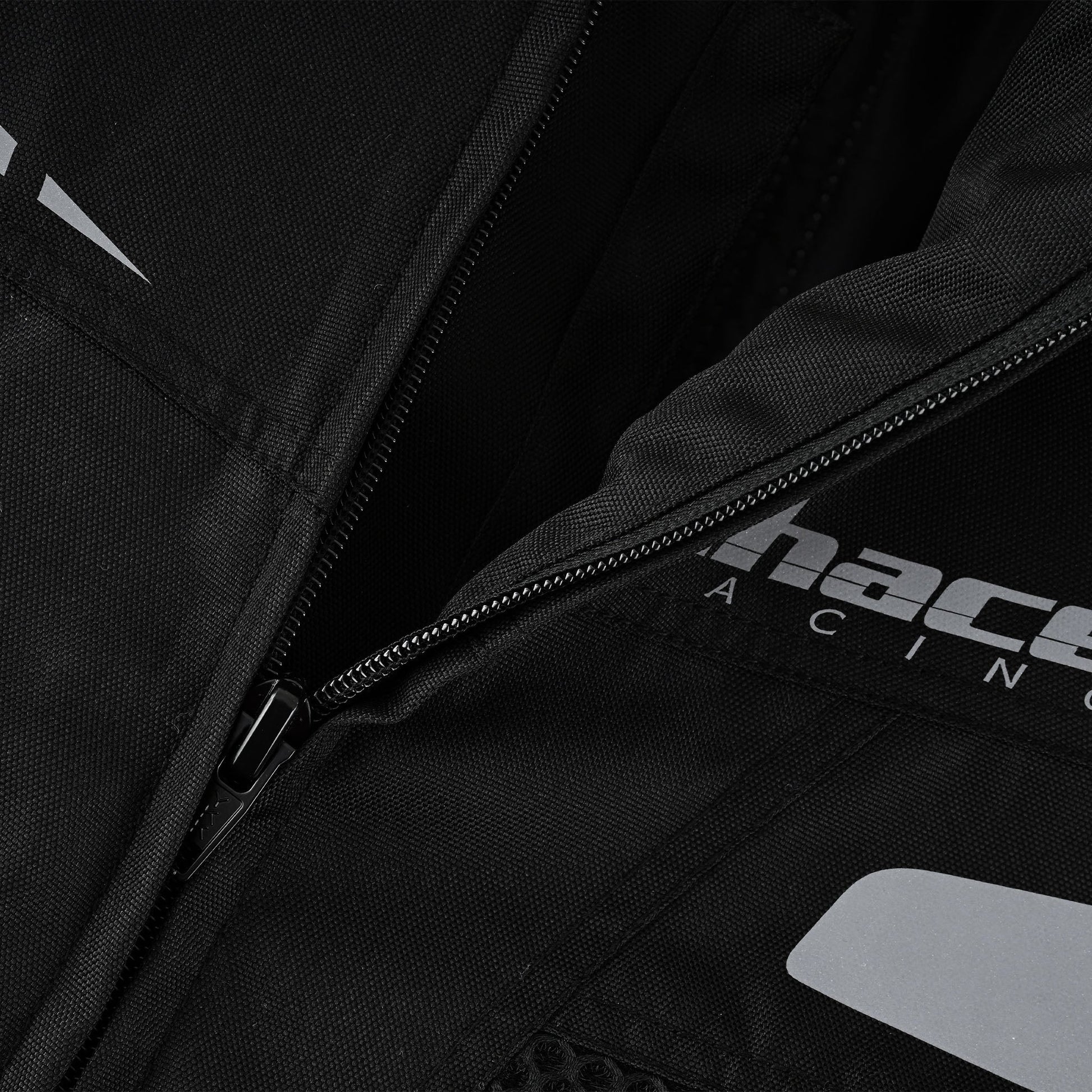 Close-up of the jacket's main front zipper area, showing the bottom of the durable zipper track and the reflective Chace Racing logo branding printed near the hem.