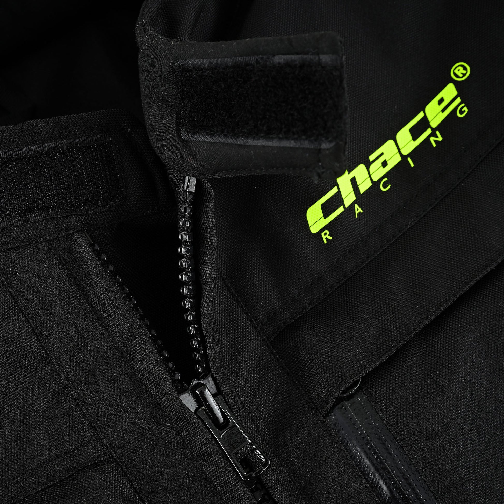 Close-up of the jacket's upper chest and collar area, showing the main heavy-duty zipper, the hi-vis yellow Chace Racing logo, and the adjustable hook-and-loop (Velcro) collar closure.