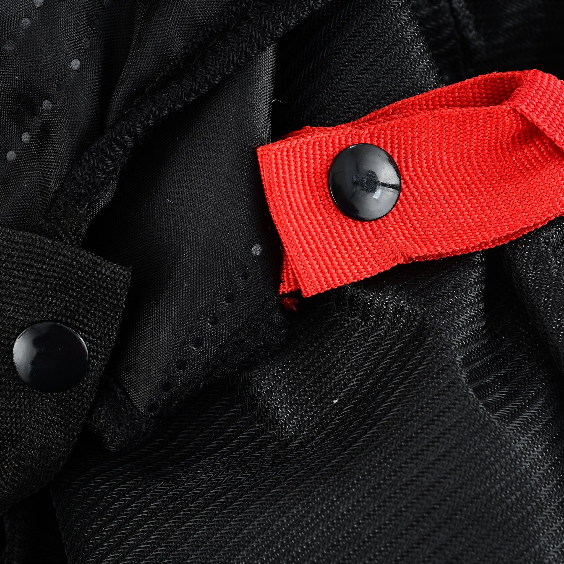 Close-up of an internal closure point showing a black snap button on a bright red webbing strap, contrasting sharply with the black textile and mesh.