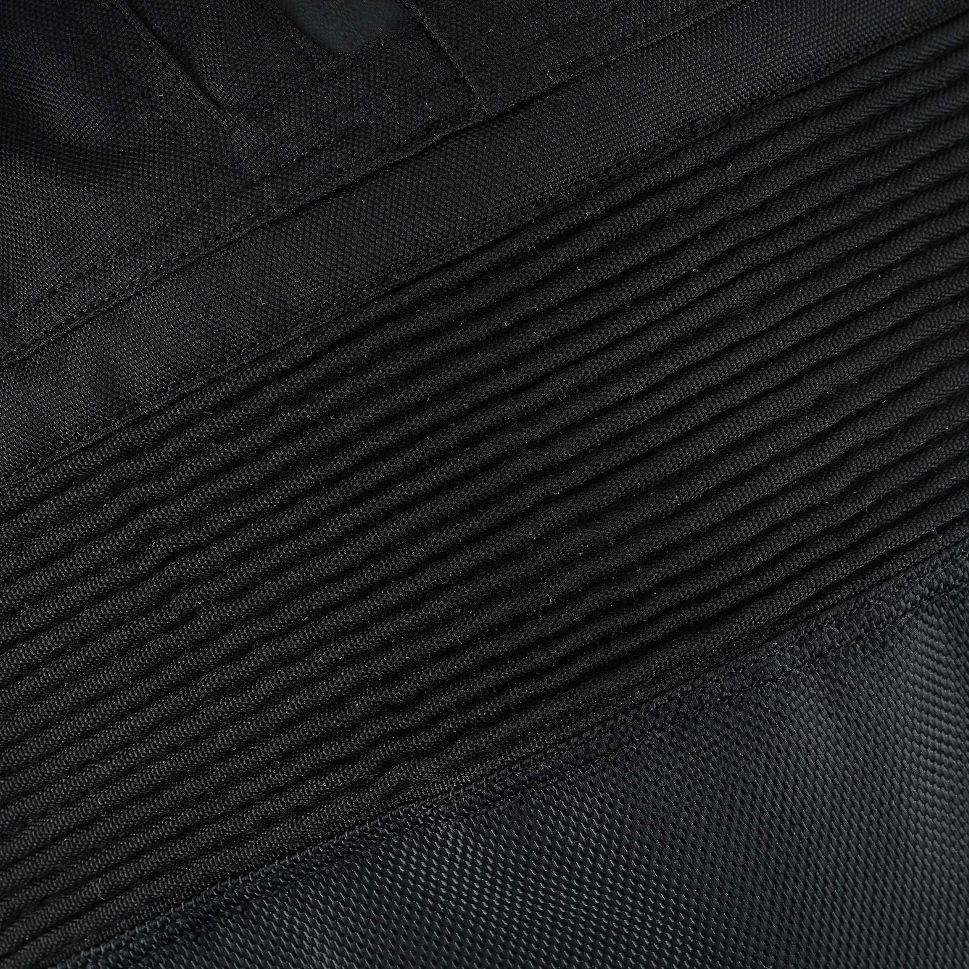 Extreme close-up of the black textile material, highlighting the ribbed, finely stitched accordion stretch panel above the knee for riding mobility.