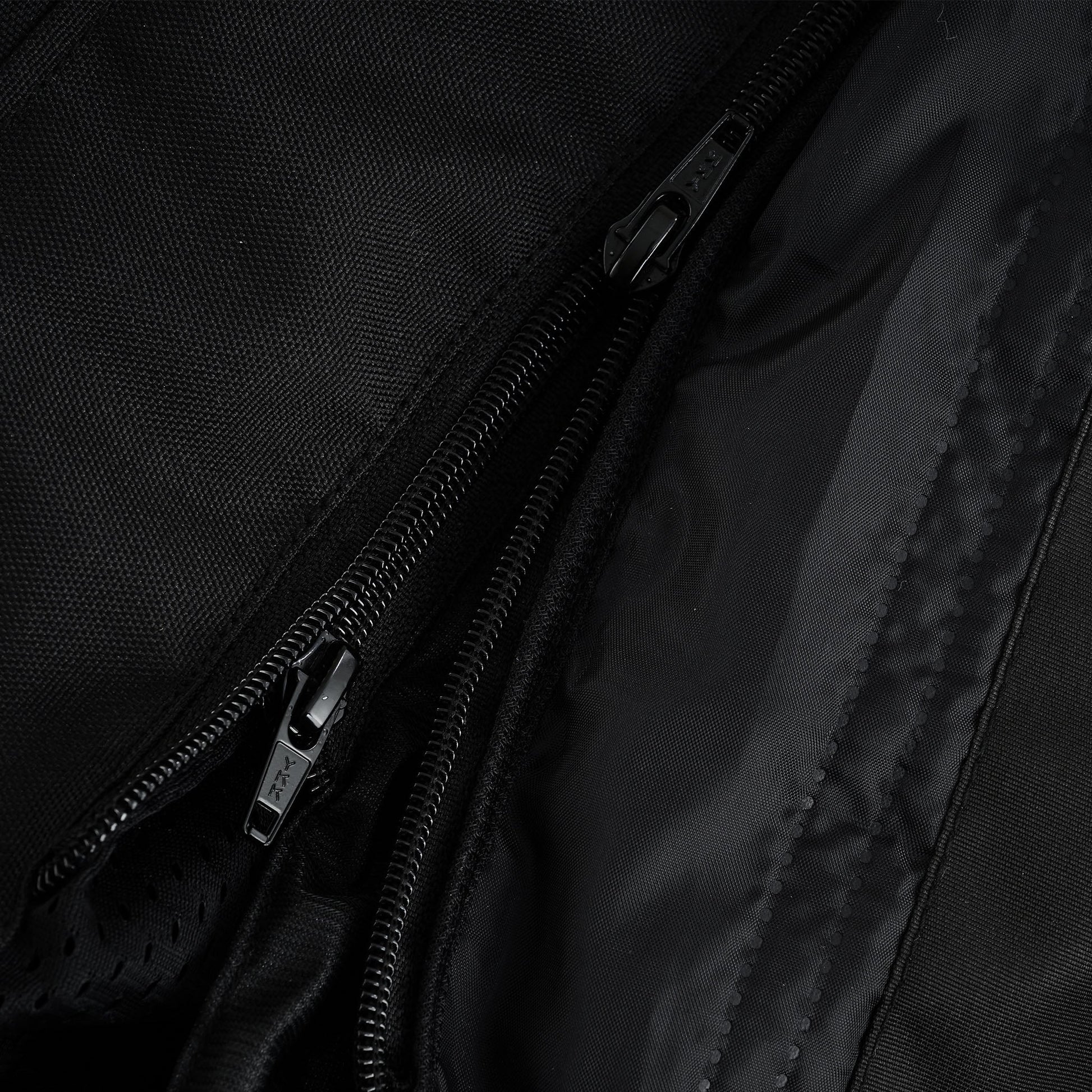 Extreme close-up of three parallel black zippers, indicating a triple-zipper system for the main closure, a storm flap, and a removable liner attachment.