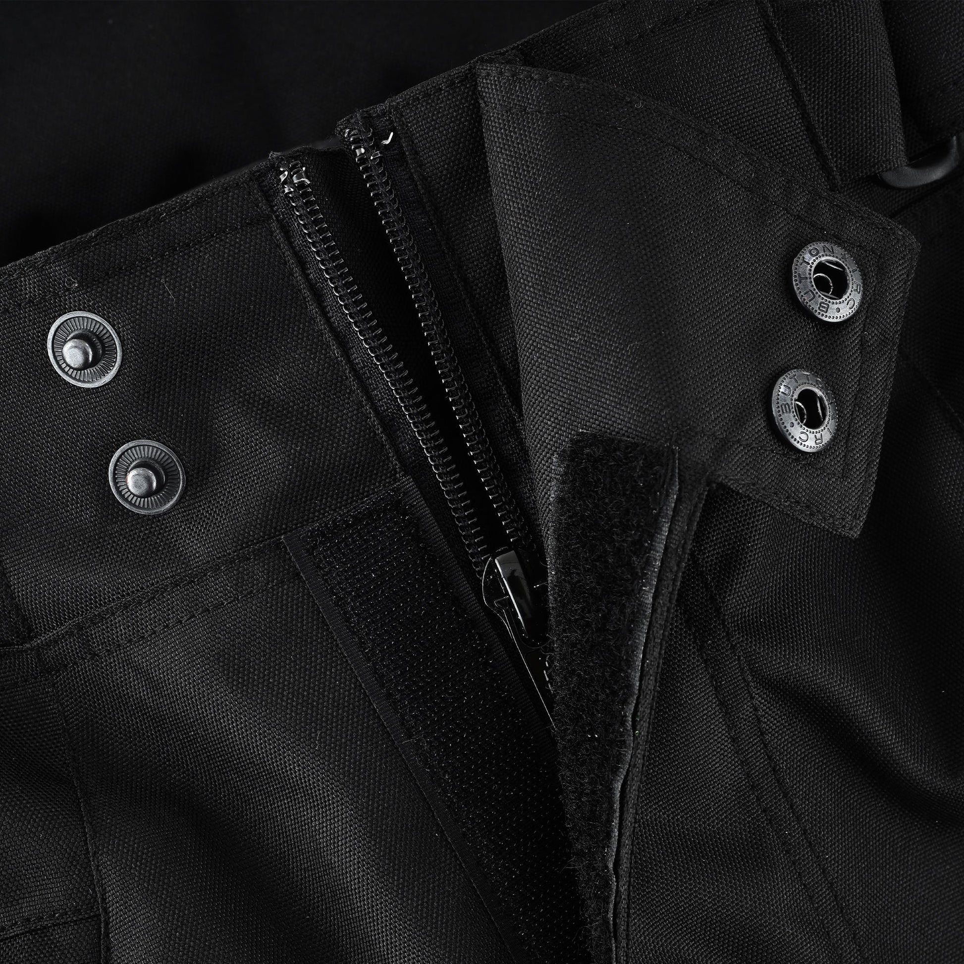 Close-up of the trousers' front waist closure, detailing the main zipper, the inner snap buttons, and the external hook-and-loop (Velcro) fastener for a secure fit.