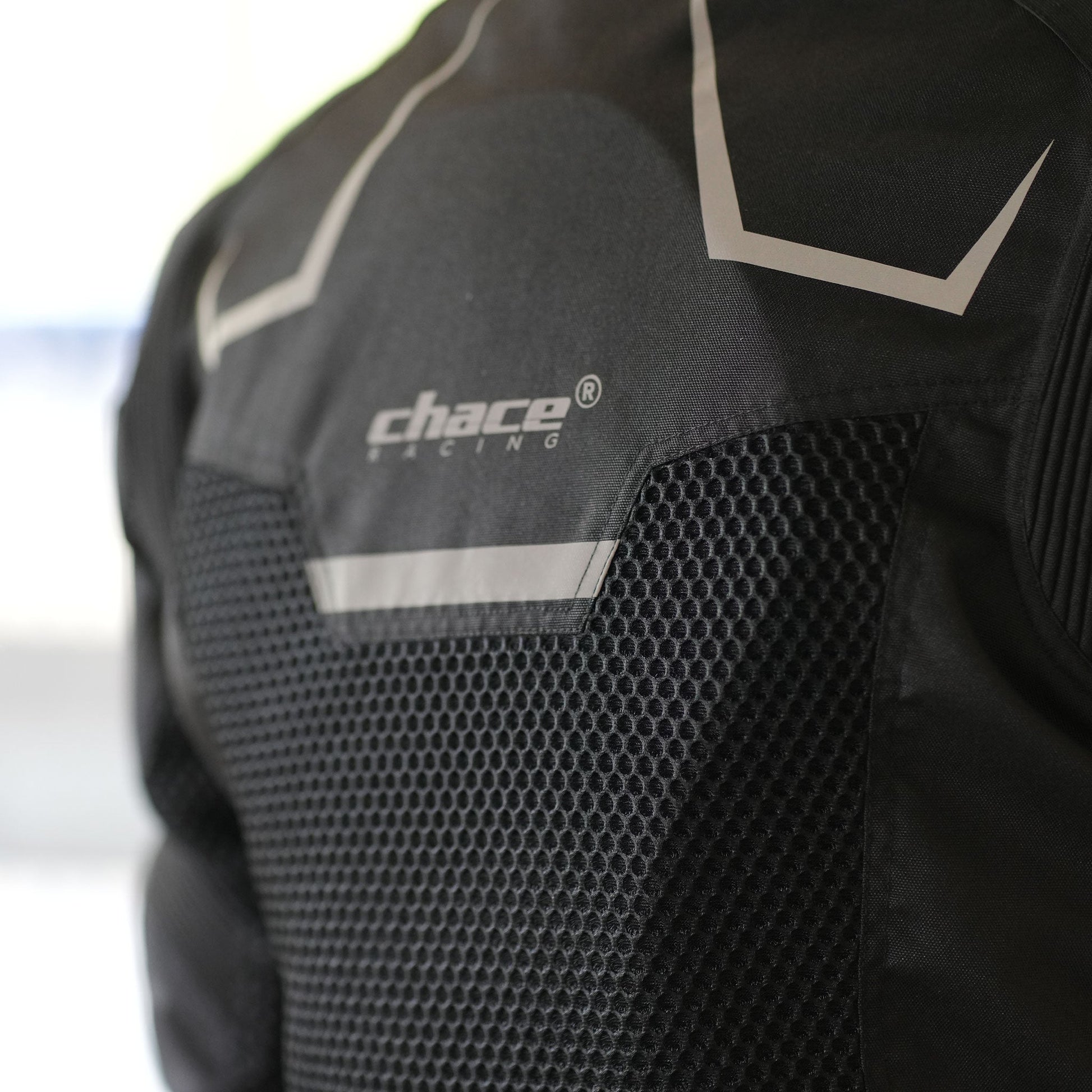 Close-up of the rider's upper back wearing the Chace Volt jacket, focusing on the large hexagonal mesh panel, the reflective horizontal strip, and the "Chace Racing" logo.