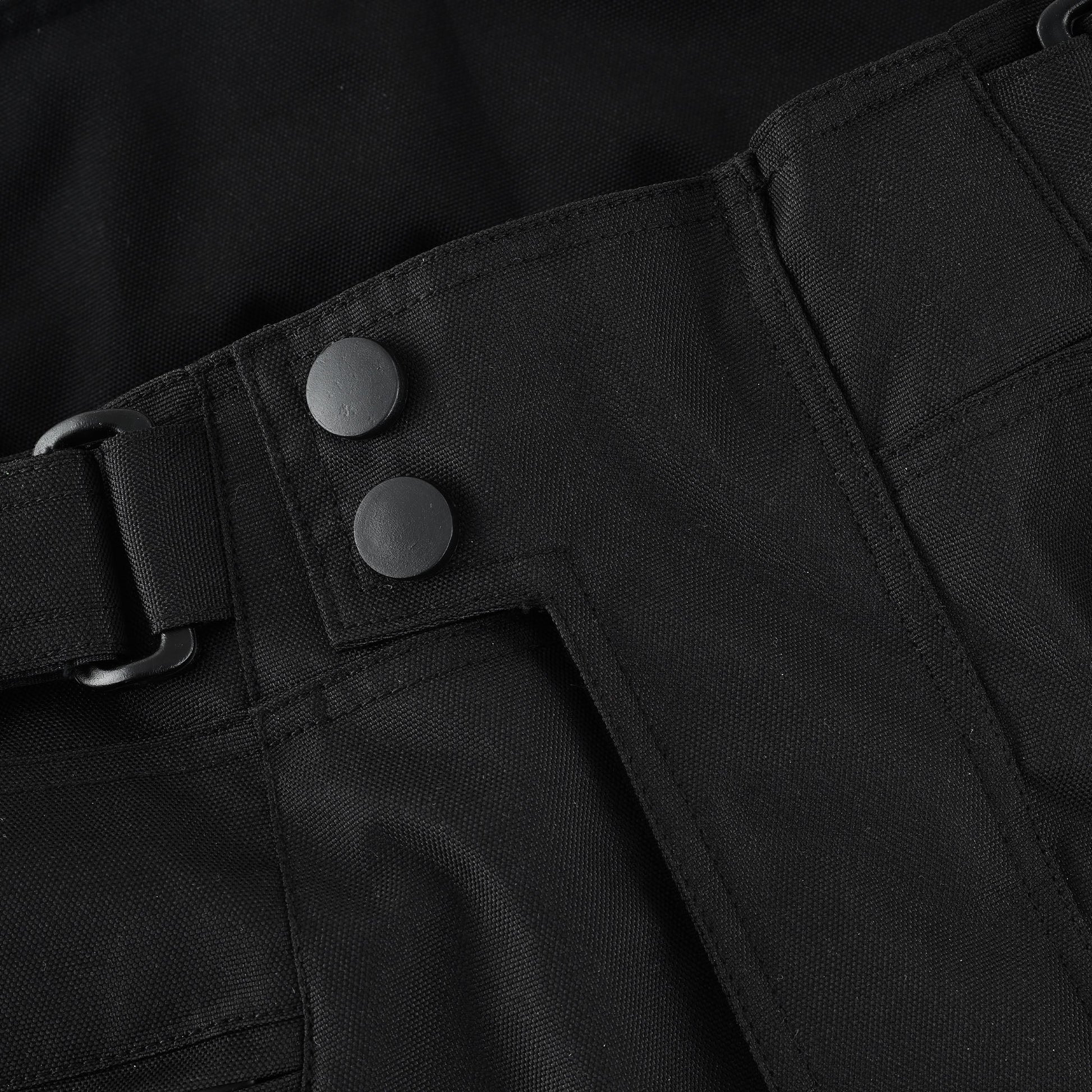 Close-up of the trouser's front waist, showing the dual large black snap buttons and the side adjustment strap secured by a black buckle.