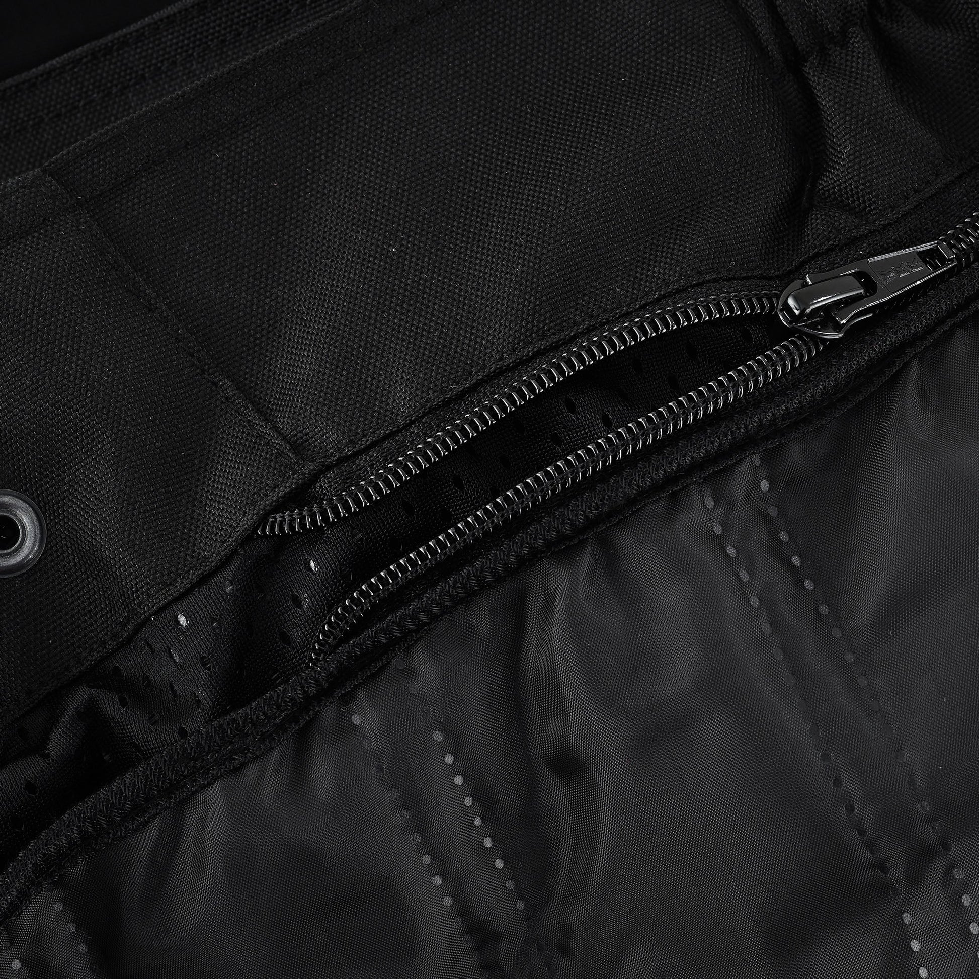 Close-up of the trousers' waist interior, showing a long zipper track used to attach the removable thermal or waterproof lining, with a perforated inner material visible.